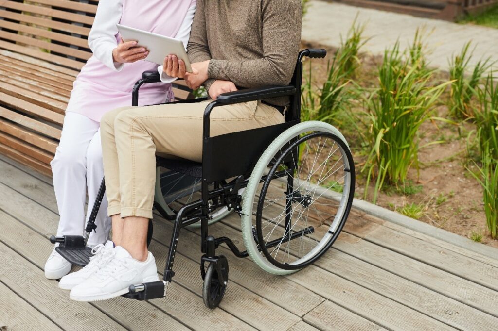 person in a wheelchair outside next to wooden garden bench 